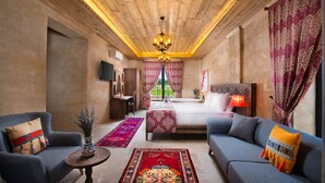 A modern bedroom with a wooden ceiling, a large bed, two sofas, a TV, and a view of the outdoors. - Cappadocia Pyramid Stone House (Nevsehir)