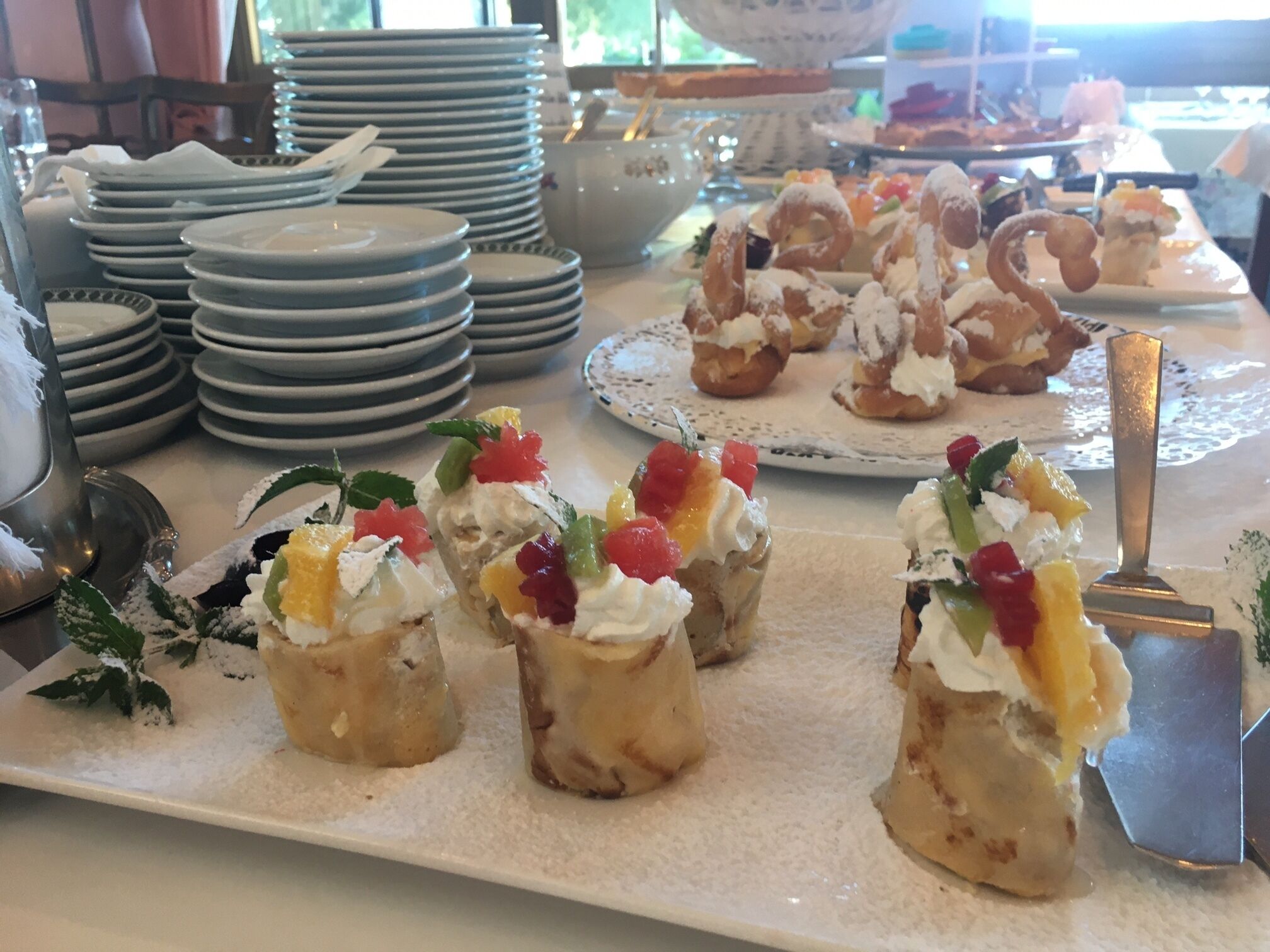 A buffet table with various desserts, including cream puffs and fruit-topped pastries, arranged on plates.