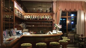 Un'area bar con un bancone in legno, diversi sgabelli, scaffali pieni di bottiglie e vista all'esterno attraverso una finestra.