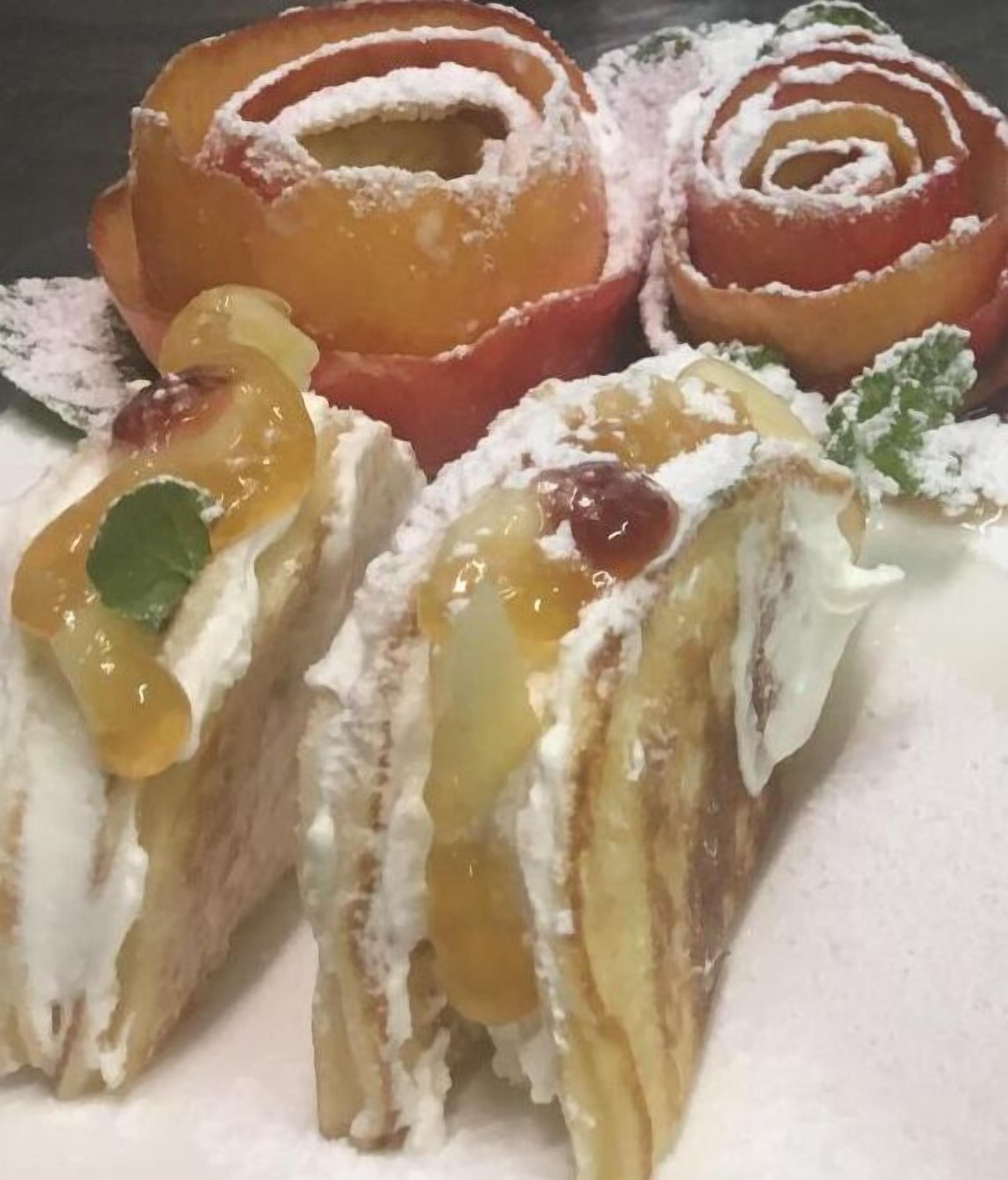 Uma sobremesa com camadas, possivelmente um bolo ou pastelaria, recheada com um creme e coberta com uma compota ou cobertura de fruta.
