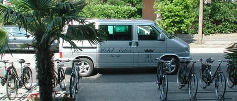A white van parked in front of a building with a balcony, surrounded by greenery and bicycles.