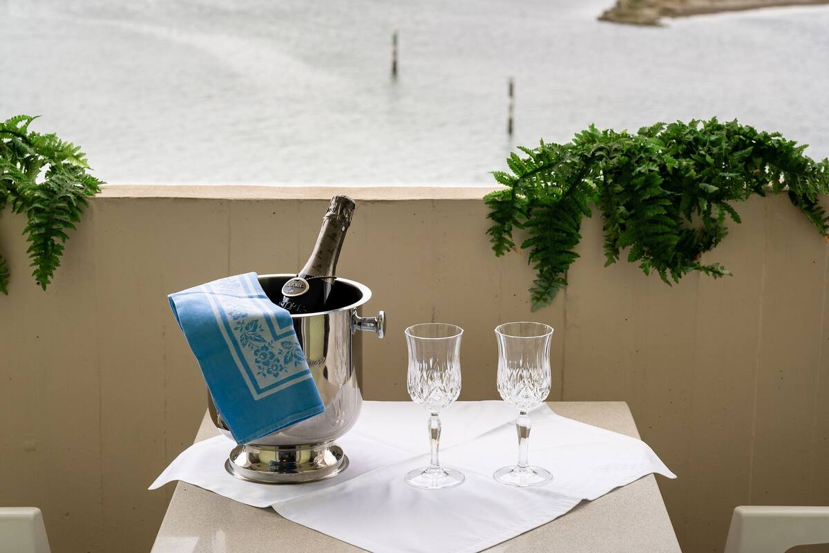 A table with a champagne bucket, two glasses, and a view of a body of water.