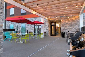 Eine Terrasse im Freien mit einer Steinwand, Holzboden und Lichterketten sowie einem Grill.