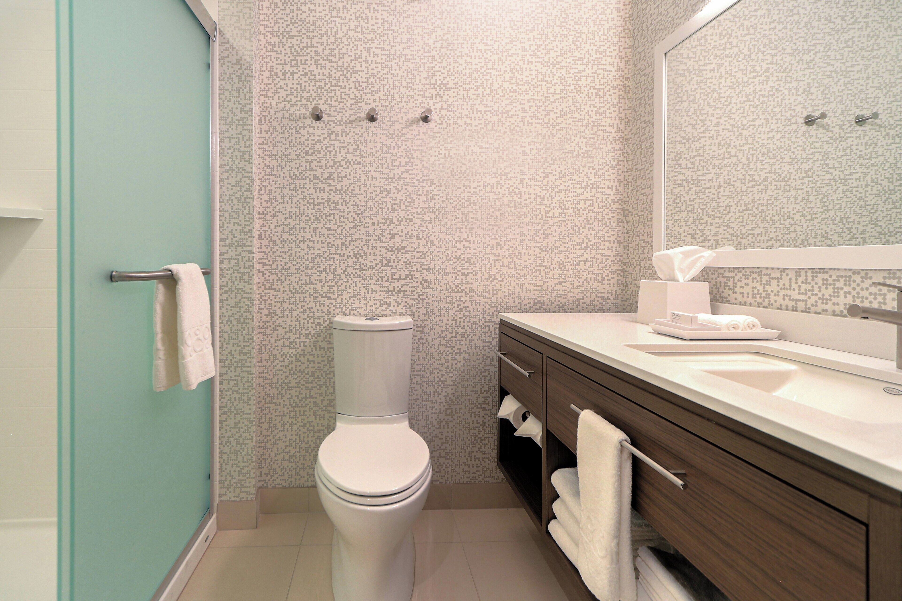 A bathroom with a toilet, a sink, a mirror, and a shower area.