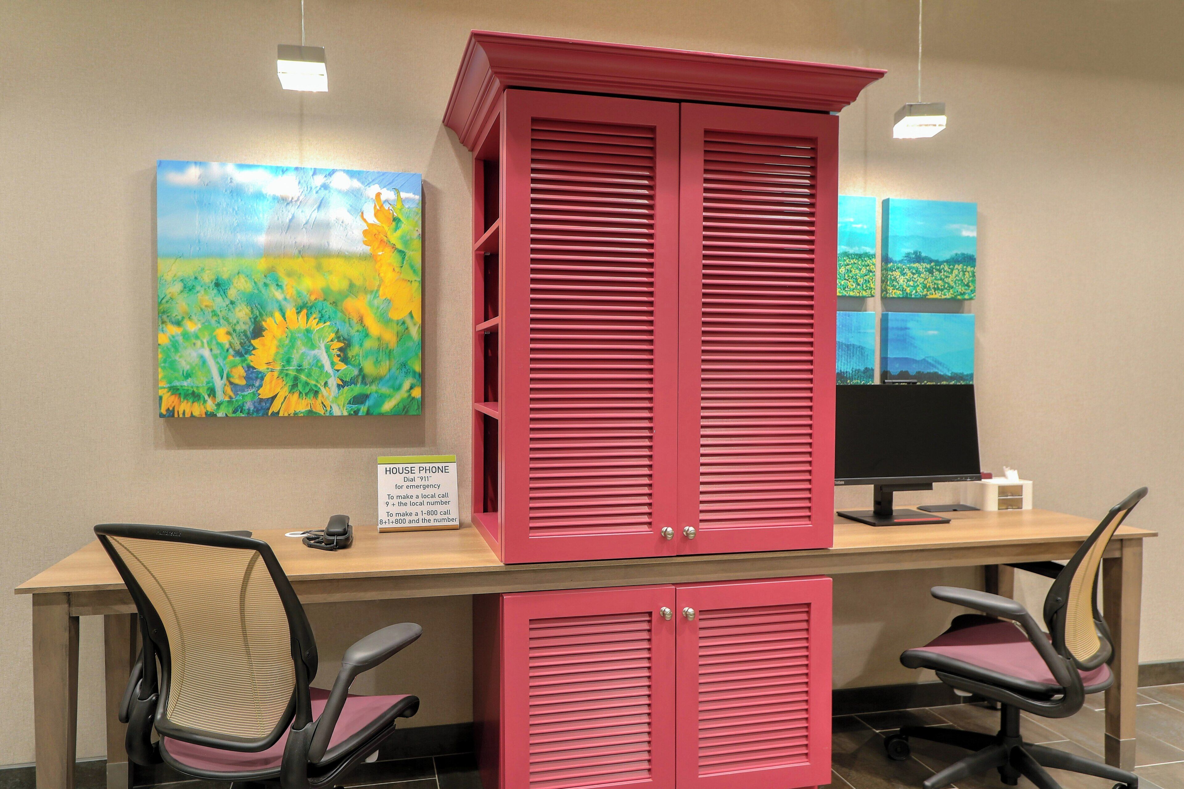 A reception desk with a computer, two chairs, a painting, and a sign indicating a house phone.