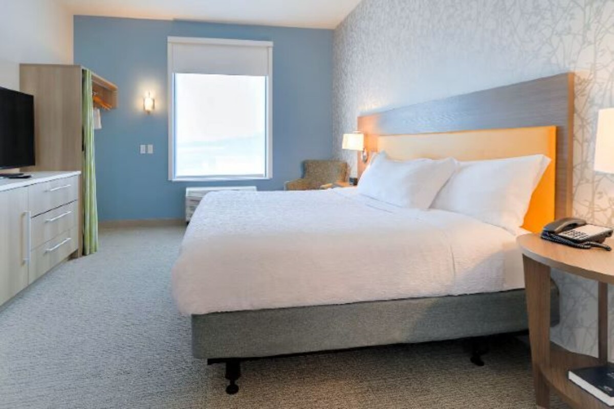 A hotel room with a bed, bedside table, lamp, and a television on a dresser.
