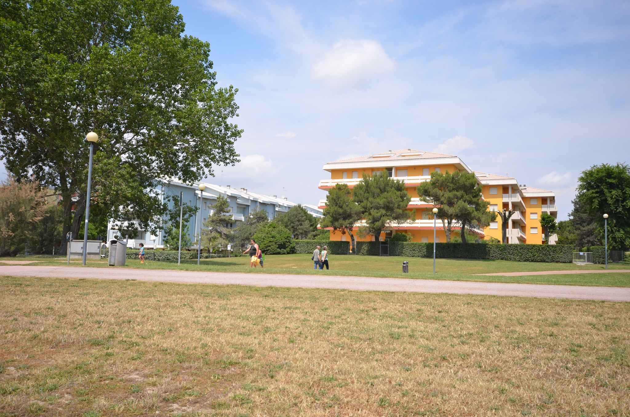 A park with a pathway, trees, and a yellow building with multiple balconies.