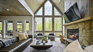 Ein großzügiger Wohnraum mit Kamin aus Stein, Ledersofas und großen Fenstern mit Blick ins Freie.