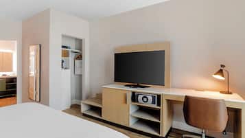 Una habitación de hotel moderna con cama, escritorio, computadora, televisor y espejo.