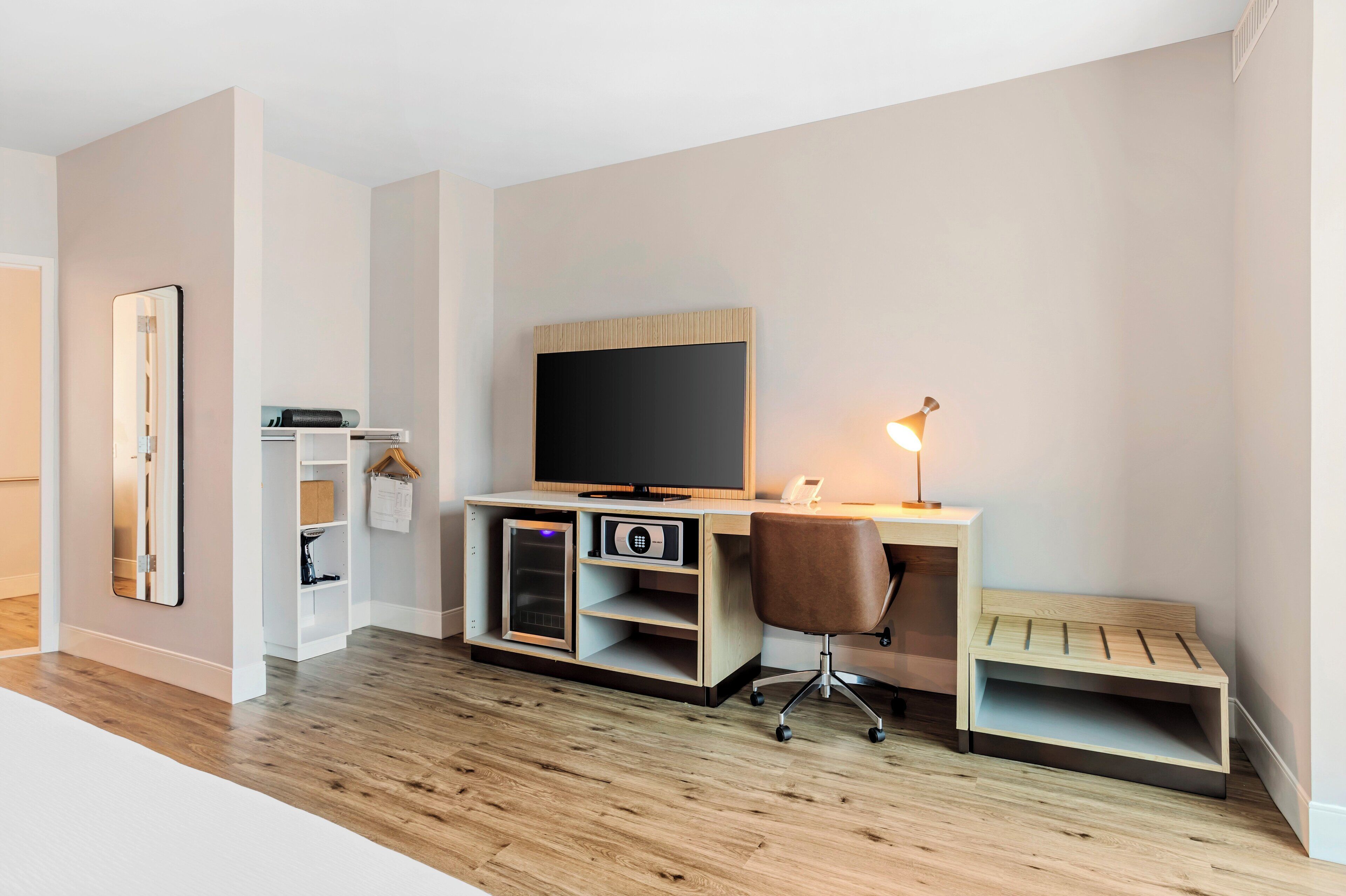 A modern bedroom with a wooden floor, a bed, a bedside table, a nightstand, and a large window.