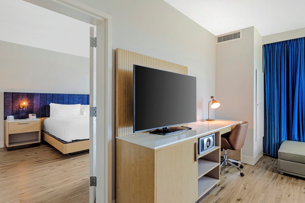 Une chambre d’hôtel avec un lit, un bureau doté d’une télévision, une chaise et une lampe de bureau.