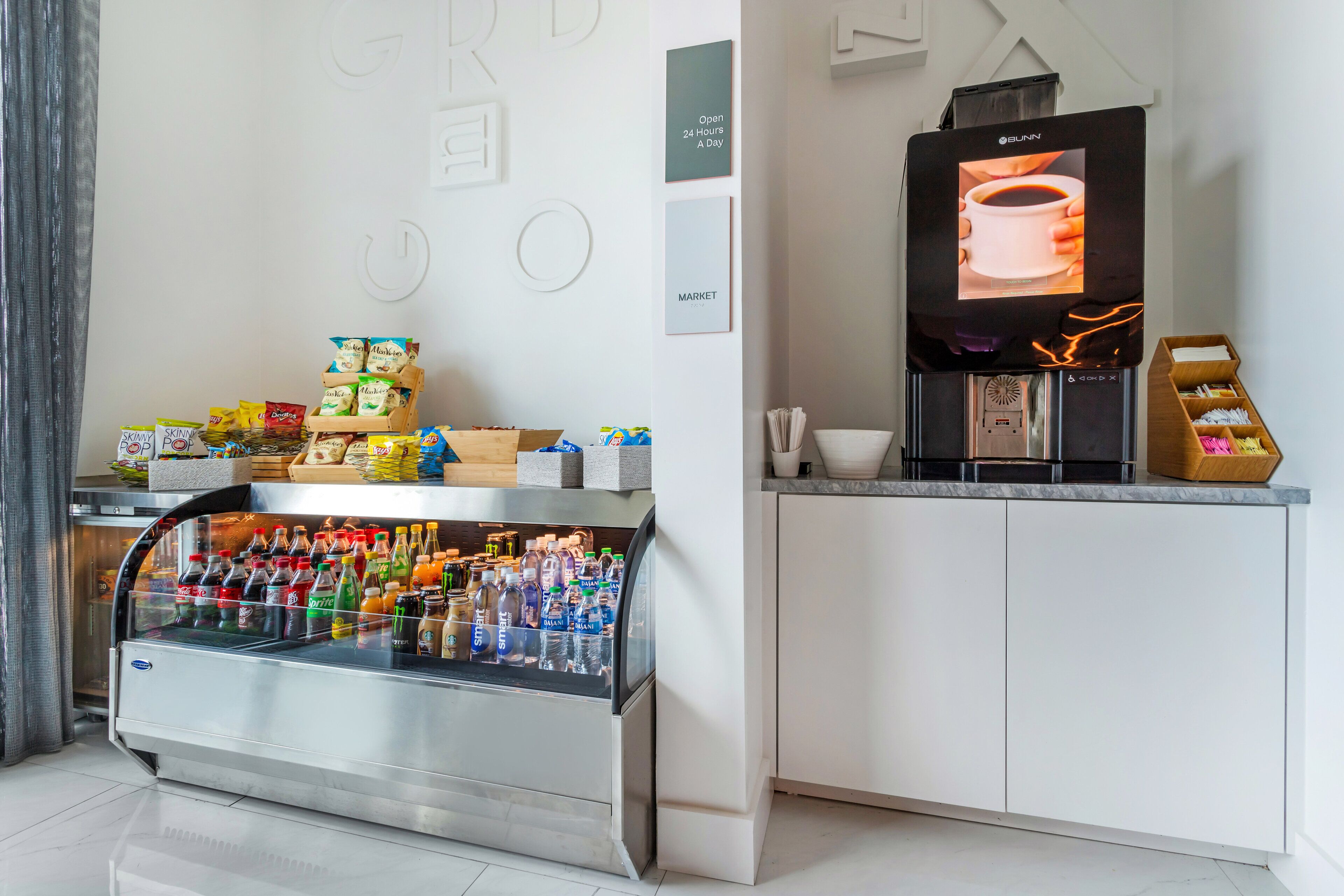Una kitchenette moderna con un refrigerador integrado, una cafetera y una variedad de bocadillos y bebidas.