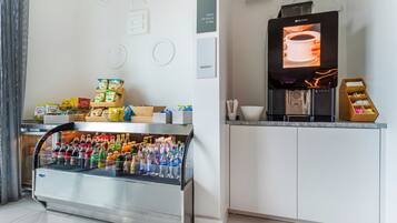 Una kitchenette moderna con un refrigerador integrado, una cafetera y una variedad de bocadillos y bebidas.