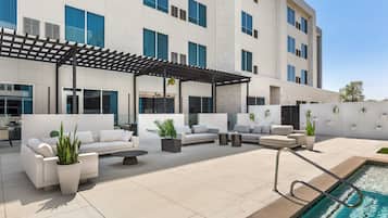 A modern outdoor patio with a pool, white sofas, and potted plants.
