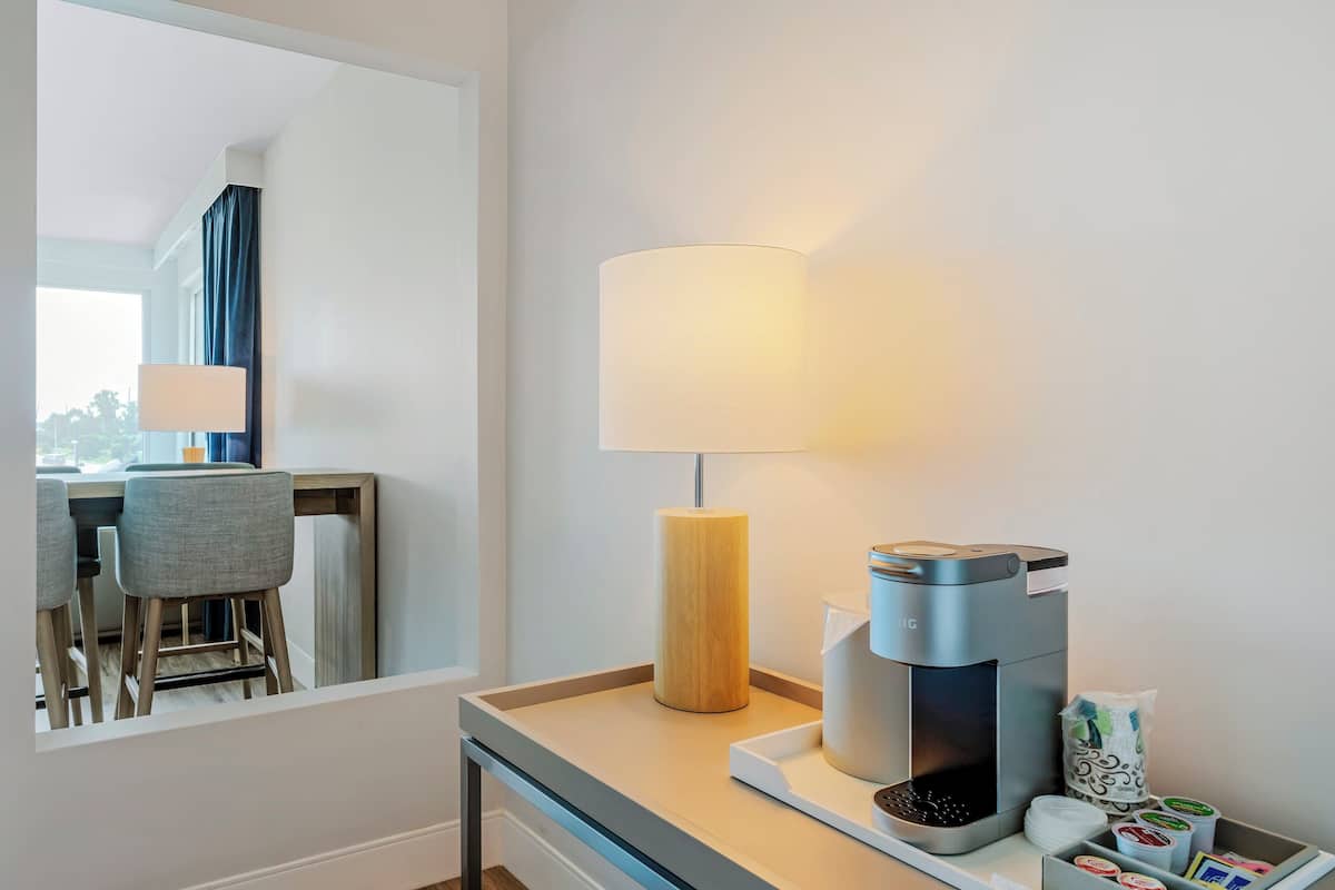 A hotel room with a desk, a lamp, a coffee maker, and a tray with coffee pods.