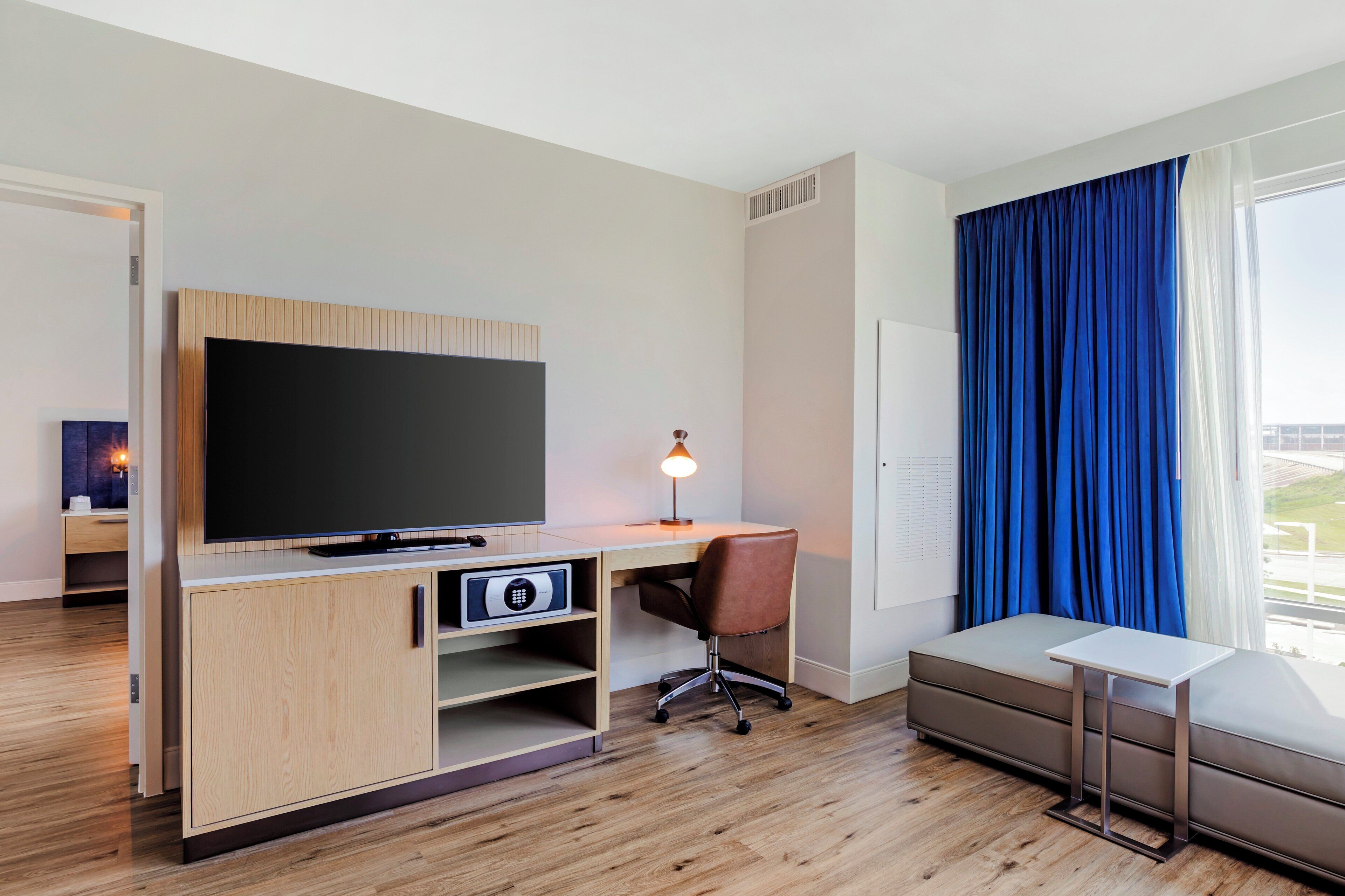 Une chambre d’hôtel moderne équipée d’une télévision à écran plat, d’un bureau en bois, d’une chaise et d’une petite table.