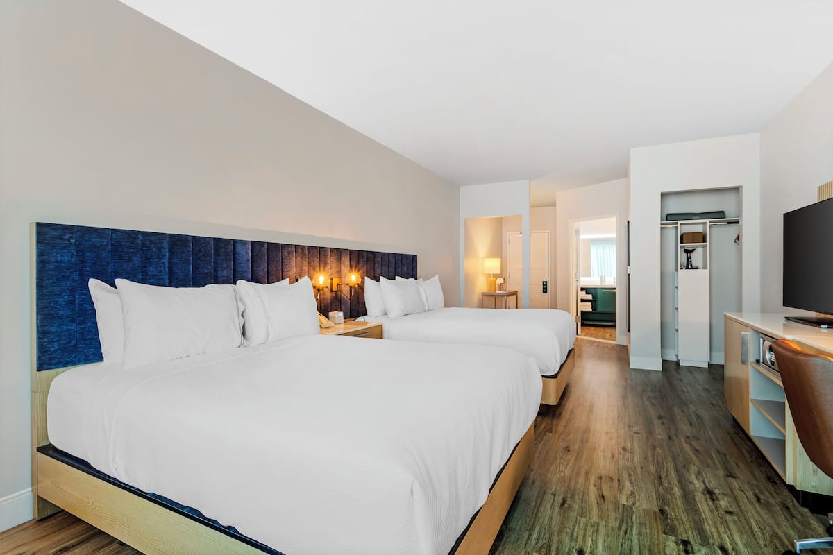 A hotel room with two beds, a TV, a desk, and a walk-in closet.