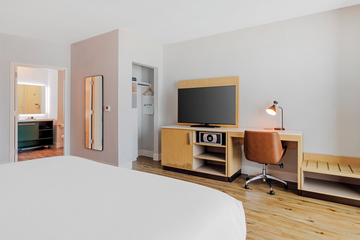 Une chambre d’hôtel avec un grand lit, un bureau en bois avec une télévision, un miroir et une petite armoire.