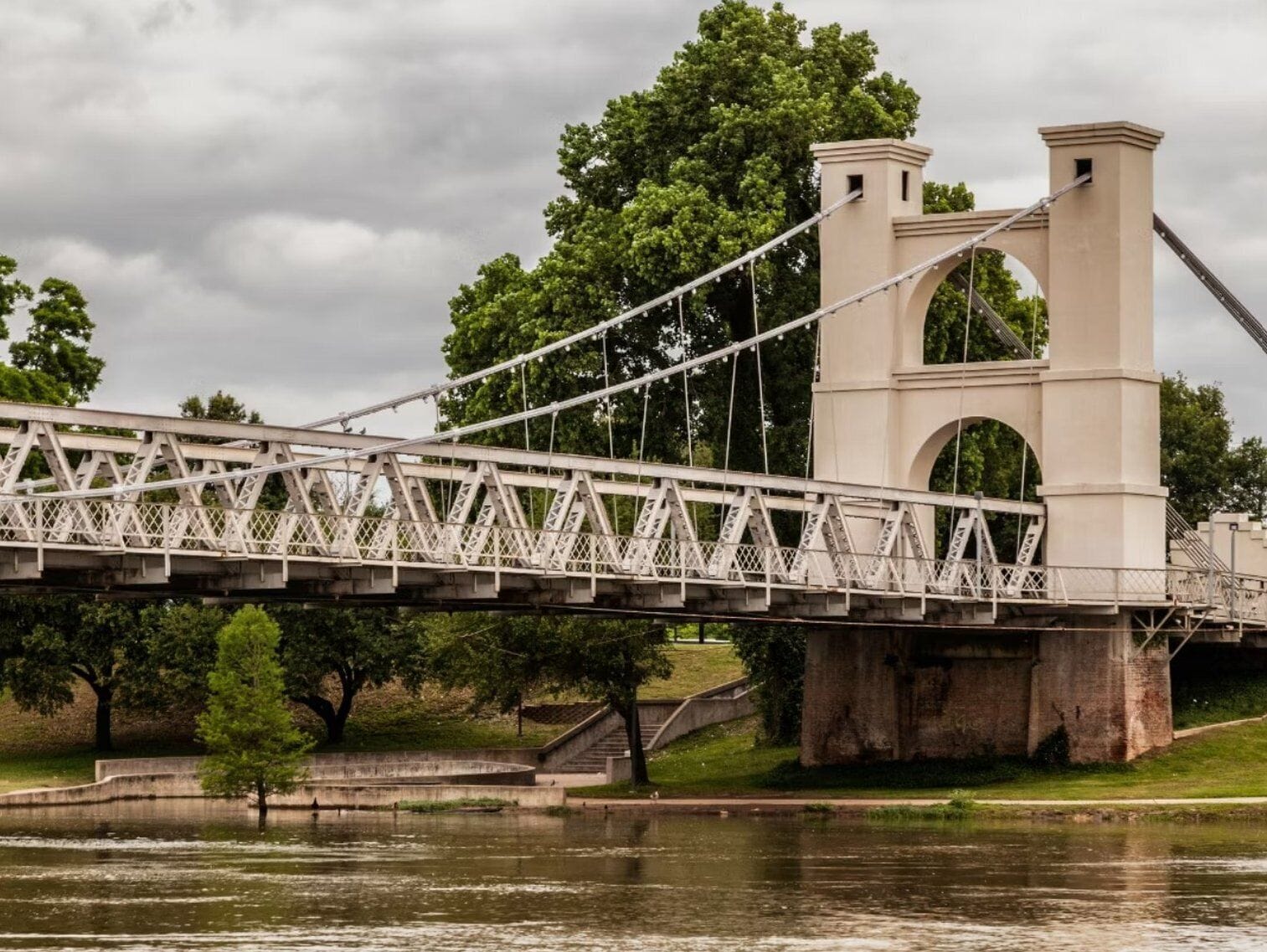 A suspension bridge with a stone tower and a river below.