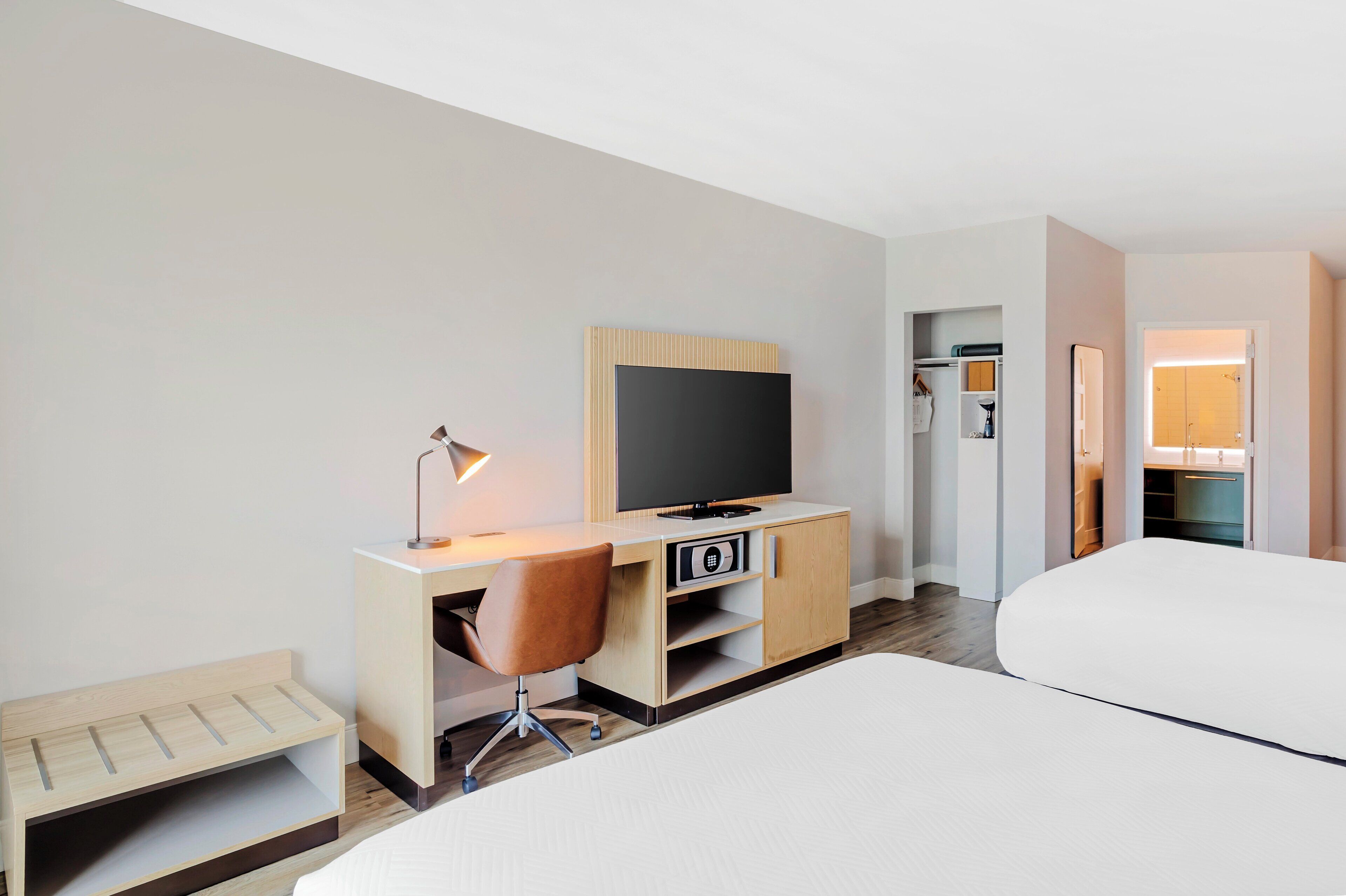 A hotel room with a bed, a desk with a TV, a chair, a lamp, and a wardrobe.