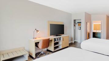 A hotel room with a bed, a desk with a TV, a chair, a lamp, and a wardrobe.