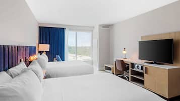 A hotel room with two beds, a desk, a television, and a large window with a view.