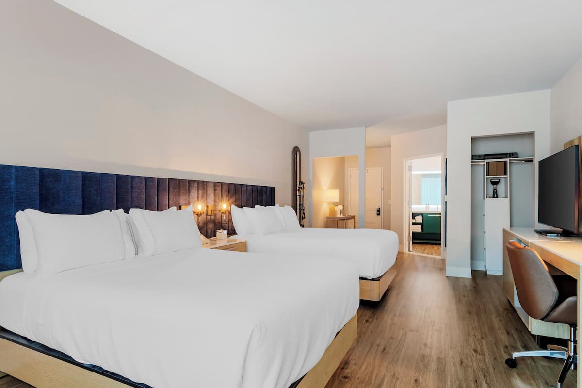 A hotel room with two beds, a desk, and a TV.