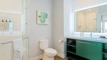 A modern bathroom with a glass shower enclosure, a white toilet, and a green vanity with a large mirror.
