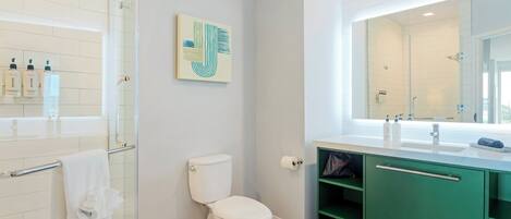 A modern bathroom with a glass shower enclosure, a white toilet, and a green vanity with a large mirror.