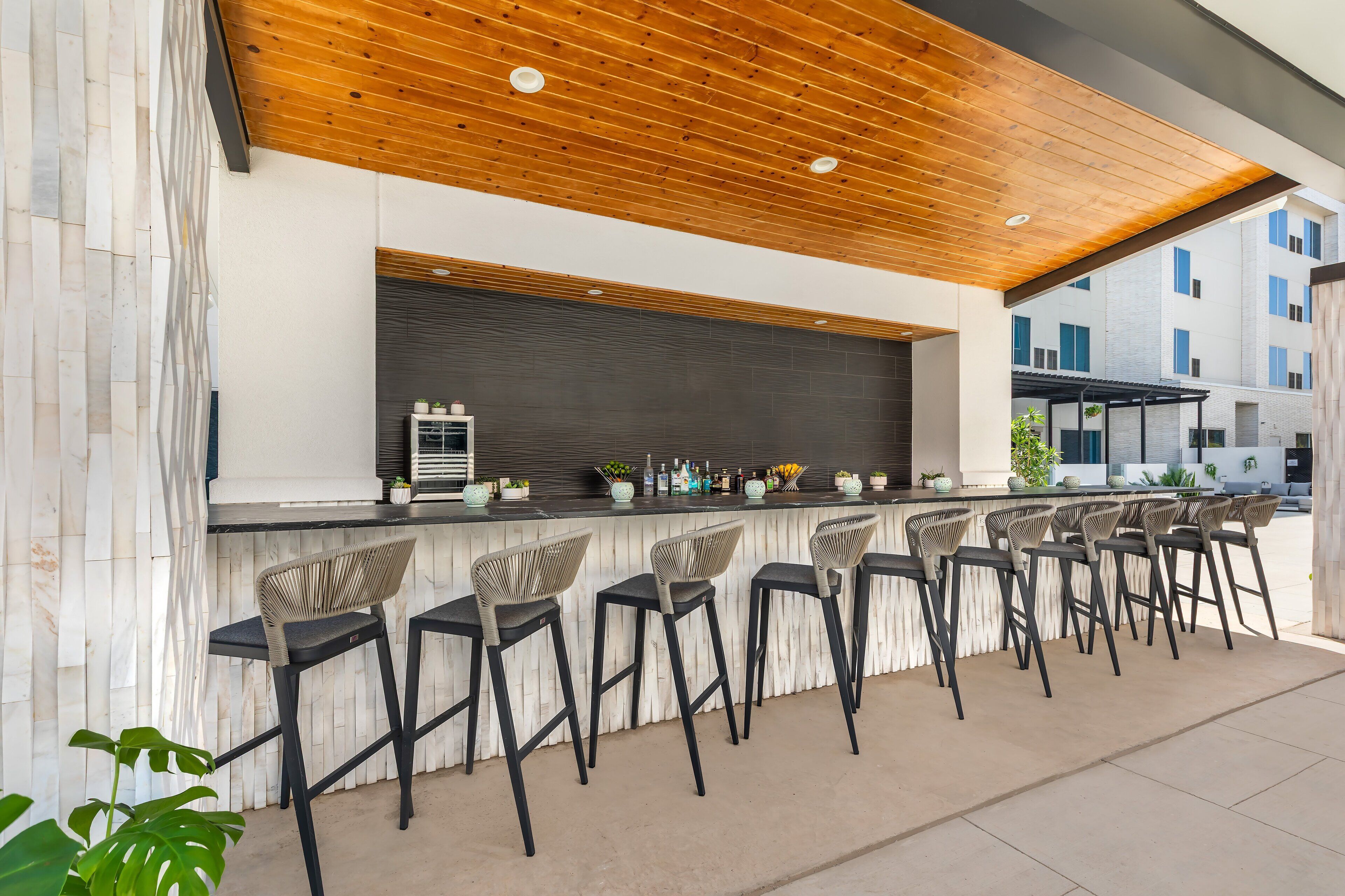 An outdoor bar area with a wooden ceiling, a stone wall, and multiple bar stools.