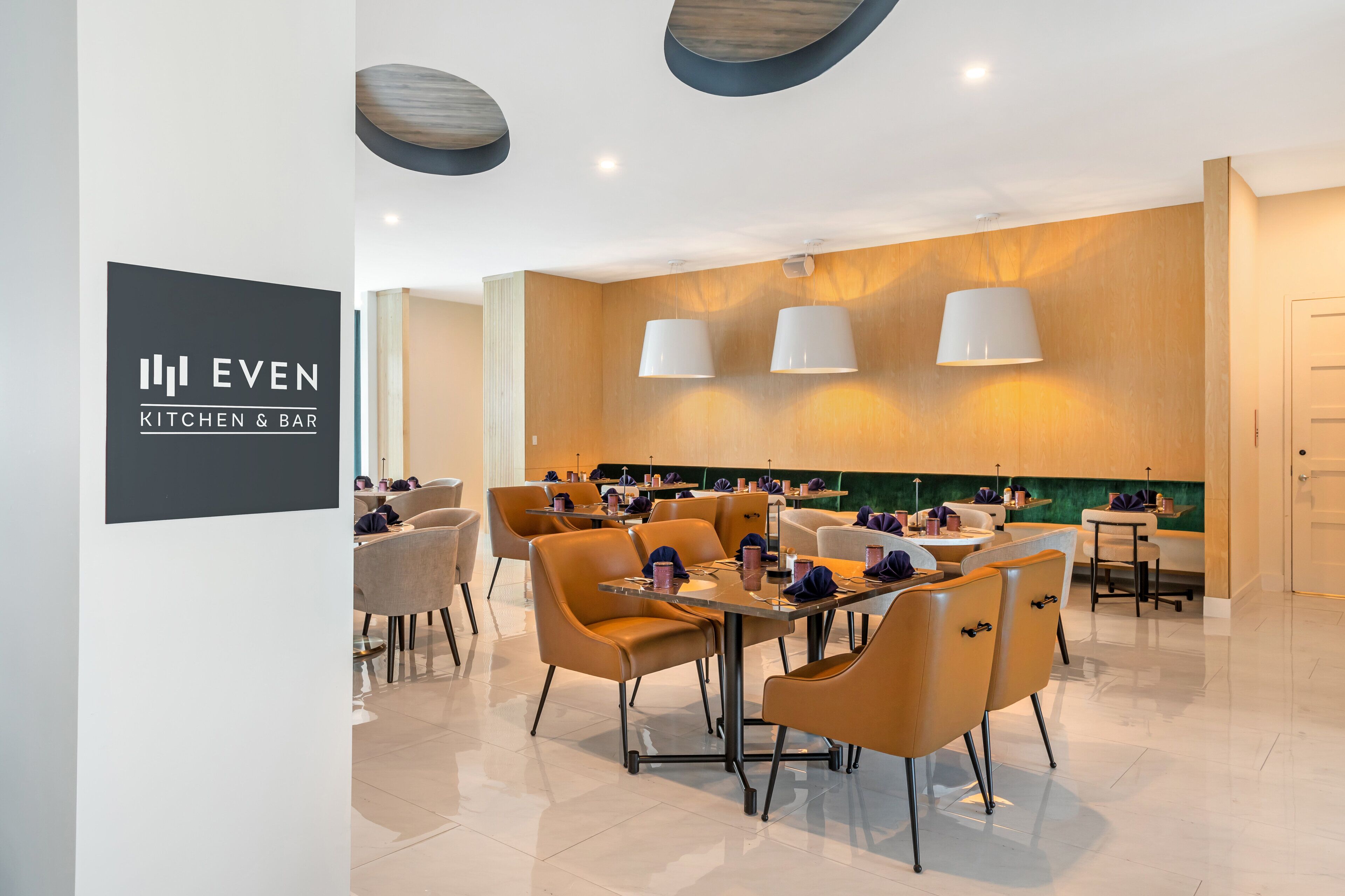 A modern restaurant with a clean, minimalist design, featuring a mix of seating arrangements and a prominent logo on the wall.