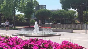 A public fountain surrounded by vibrant pink flowers, with a paved walkway and a few people in the background. - Studio MONO renovated with swimming pool and sea views (Porto Santa Margherita)