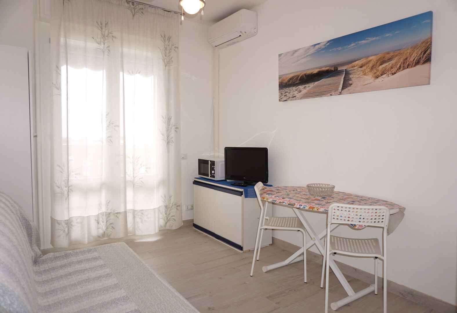 Ein kleines Zimmer mit einem Bett, einem Schreibtisch mit Computer, einem Stuhl und einem Tisch.