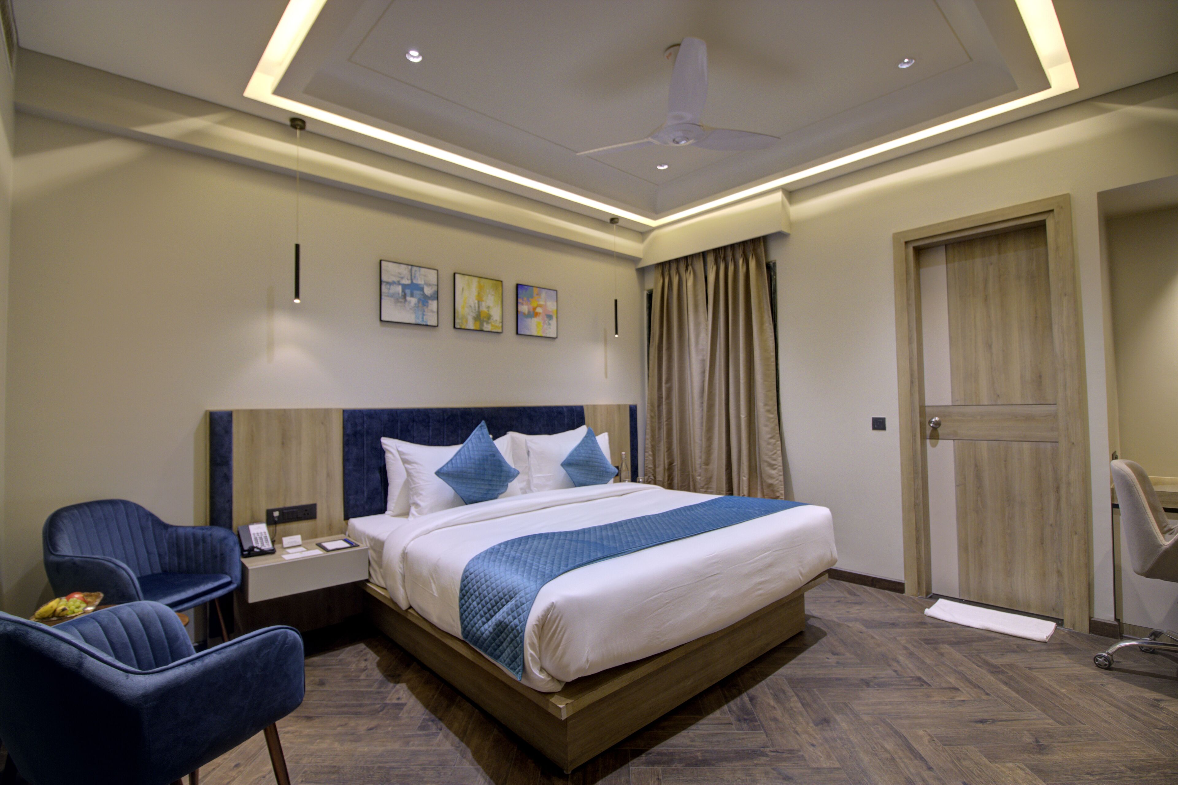 A hotel room with a large bed, a desk with a chair, a ceiling fan, and artwork on the wall.