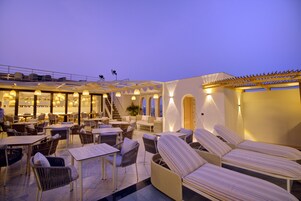 A rooftop terrace with wicker furniture, tables, and lounge chairs.