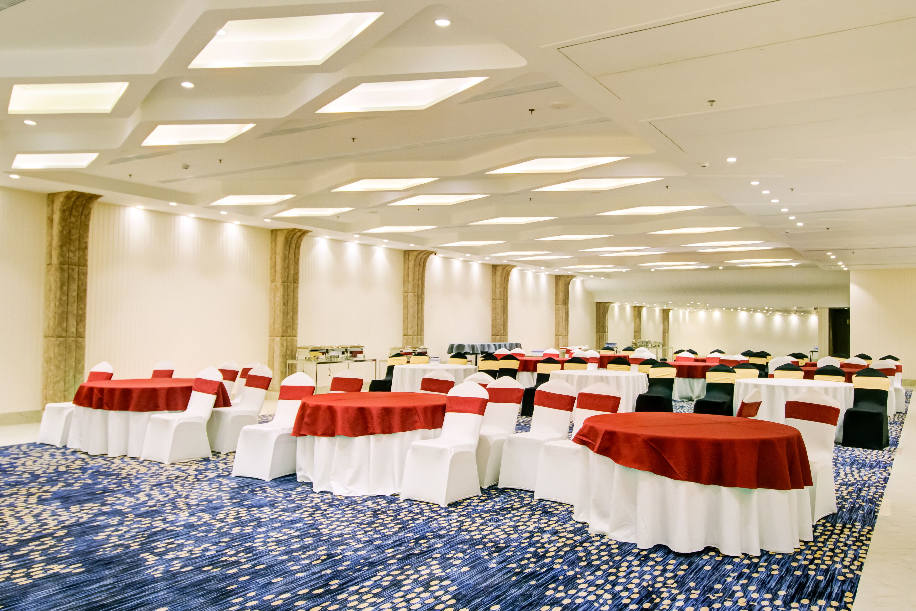 A banquet hall with round tables and white chairs, red sashes, and a patterned carpet.