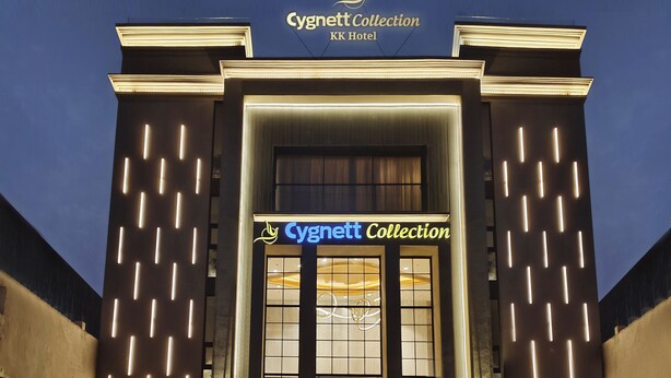Exterior do Cygnett Collection KK Hotel com linhas verticais iluminadas na fachada, uma entrada grande com portas de vidro e um letreiro acima da entrada.