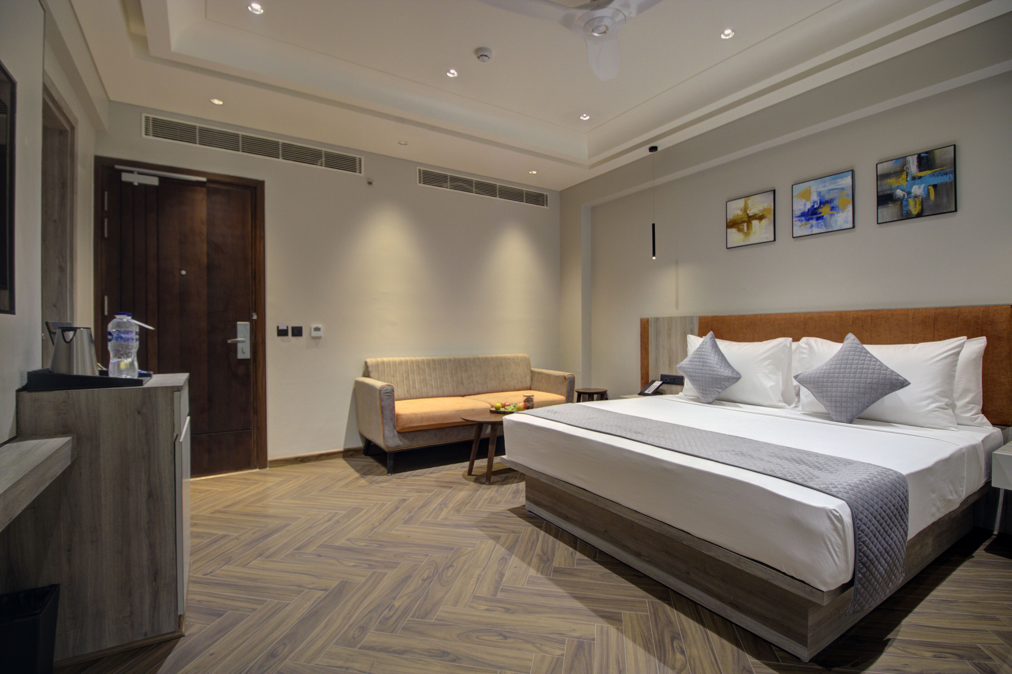 Una habitación de hotel moderna con una cama grande, un sofá, un escritorio y suelo de madera.