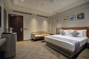 Una habitación de hotel moderna con una cama grande, un sofá, un escritorio y suelo de madera.