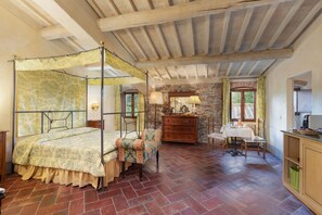 A bedroom with a four-poster bed, a wooden dresser, a dining table with chairs, and a stone wall. - Beautiful private villa with WIFI, private pool, TV, patio and panoramic view, close to Florence (Poggiolo-salaiole)