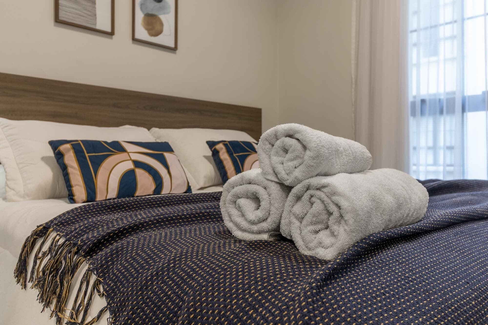 A neatly made bed with rolled towels, pillows, and a dark patterned blanket.