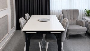 A modern dining room with a rectangular table, six chairs, a grey sofa, and a large window with sheer curtains. - Lumiera Suites Hotel (Bursa)