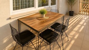 A patio with a wooden table and four chairs, large windows, a potted plant, and a view of buildings. - Lumiera Suites Hotel (Bursa)