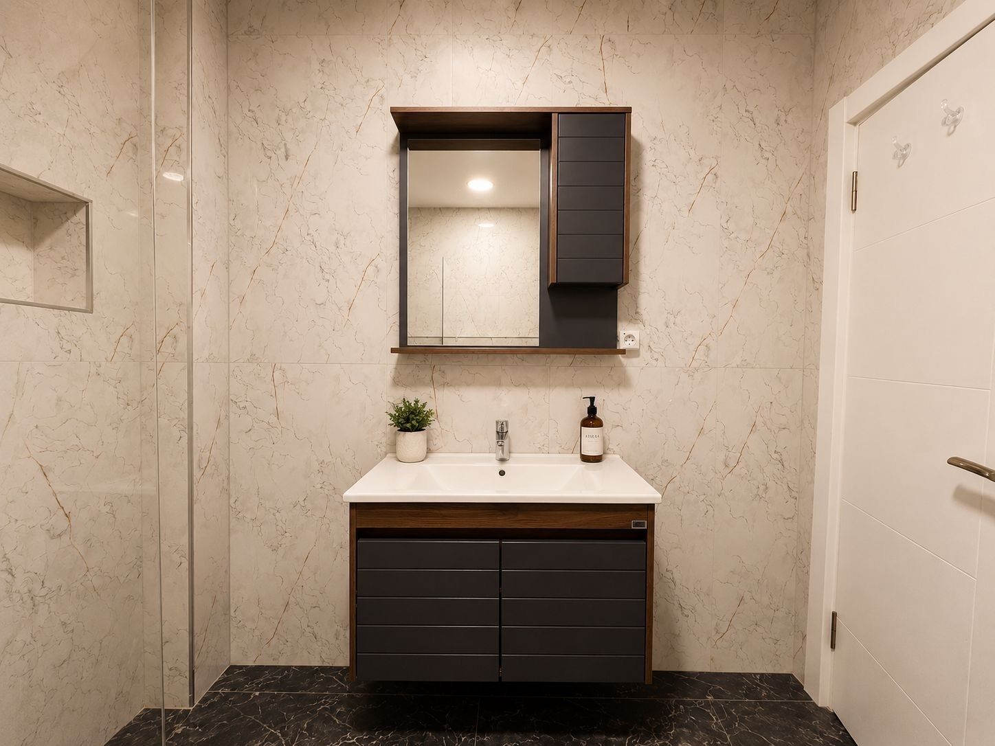 A bathroom with a marble wall, a sink with a wooden cabinet below, and a mirror above.