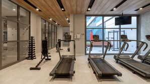 Ein modernes Fitnessstudio mit Laufbändern, Kraftgeräten und einem großen Fenster mit Blick ins Freie.