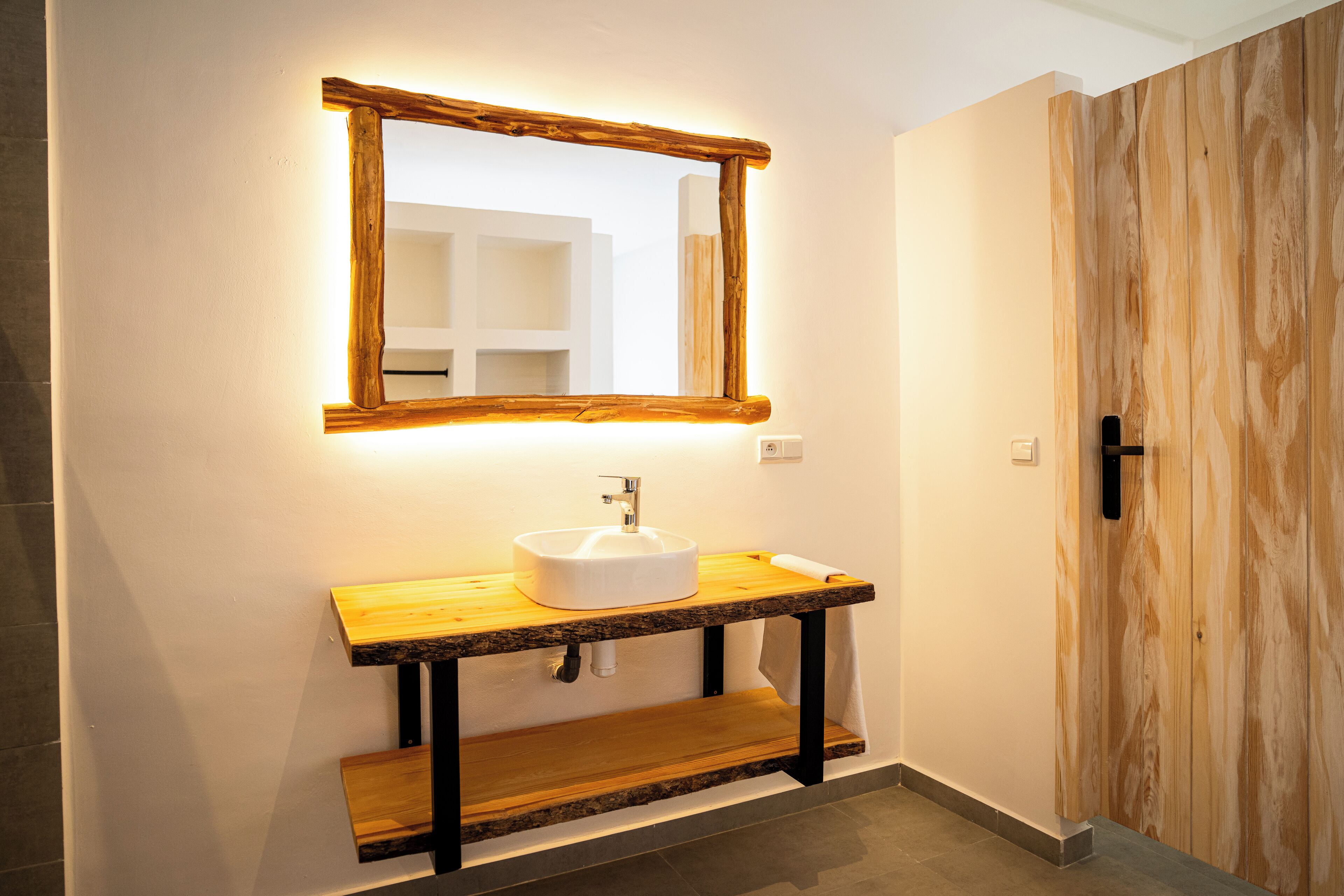 A bathroom with a wooden vanity, a white sink, and a mirror with a wooden frame.