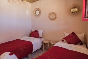 Una habitación con dos camas, cada una con ropa de cama roja y blanca, y pequeñas mesitas redondas.