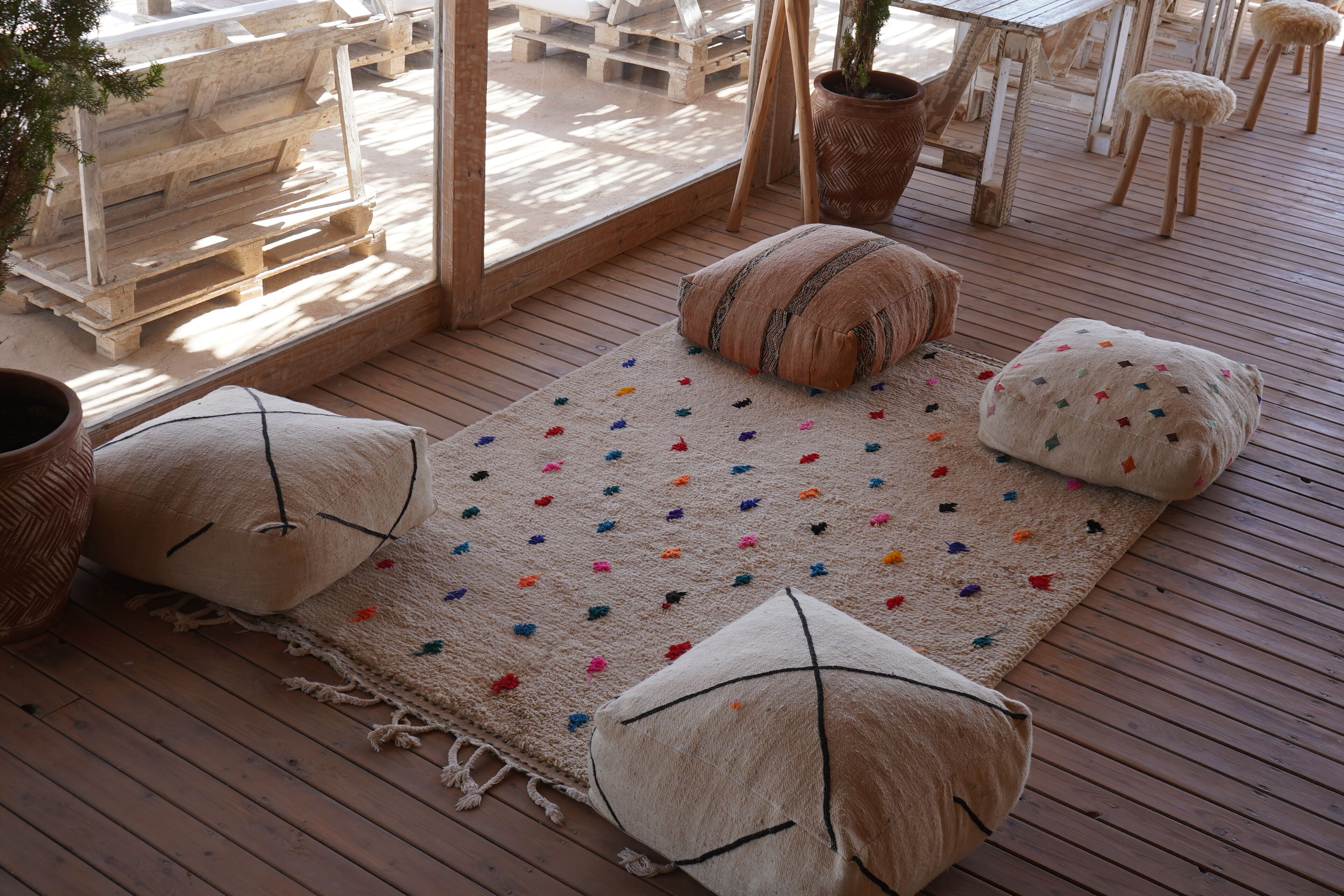 Una terraza de madera con un tapete, cojines y una planta en maceta.