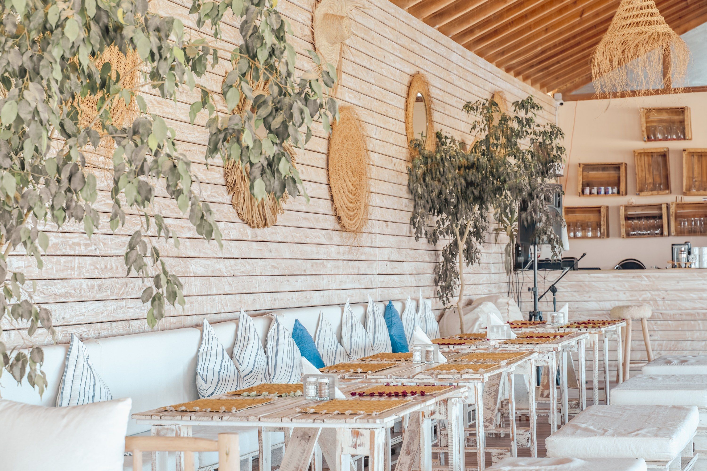 A restaurant with a long table set for dining, wooden walls, and hanging plants.