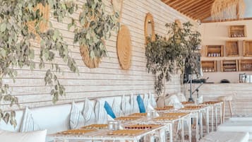 A restaurant with a long table set for dining, wooden walls, and hanging plants.